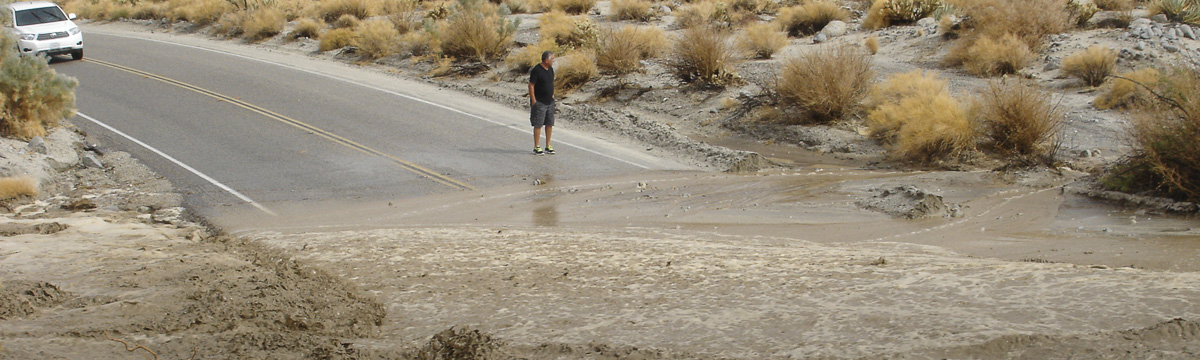 photo of flash flood running across desert road; a man stands nearby
