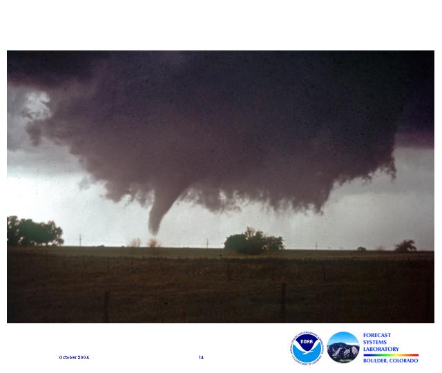 A small funnel descends nearly to the ground from a ragged wall cloud.