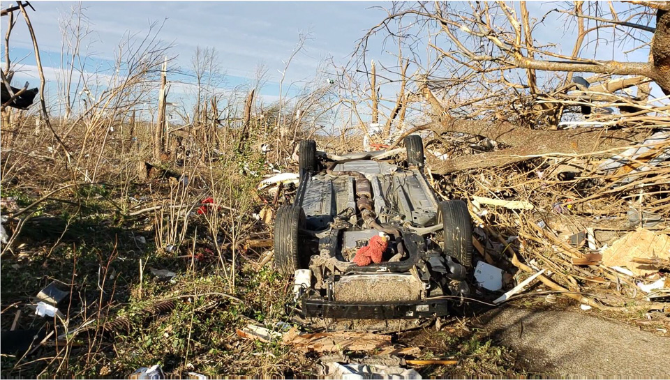 Demolished car, upside down in other debris. There is a stuffed animal on top of the car. December 2021 Kentucky outbreak damage